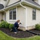 homeowner inspecting house foundation and downspout drainage system to prevent water damage and improve exterior drainage