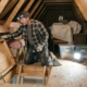 Home inspector examining attic access, insulation, wood framing, and stored items with a headlamp during a professional residential inspection