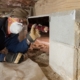 Home inspector checking crawl space foundation supports with a flashlight during a termite inspection for wood damage and pest activity